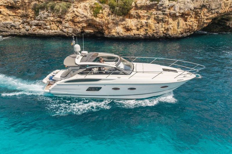 2015 Princess V39 yacht cruising in clear blue waters near rocky coastline.