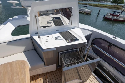 Outdoor kitchen on 2025 Princess S65 yacht with grill and storage, docked by the water.