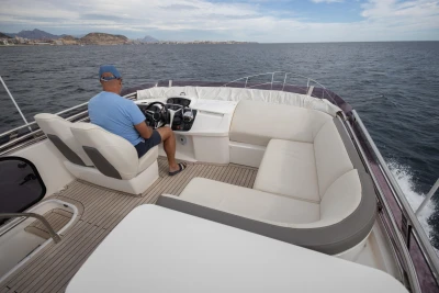 Man steering 2018 Princess 43 yacht on open sea, clear skies, spacious deck seating.