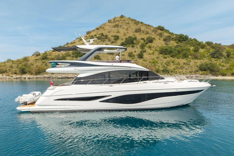 Luxurious 2025 Princess F65 yacht cruising in serene blue waters near a lush green island.