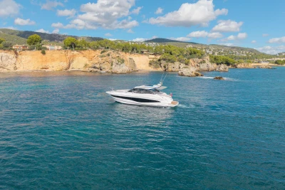 2024 Princess V50 Open yacht cruising near scenic coastal cliffs under a blue sky.