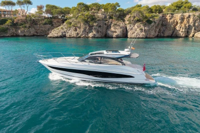 2024 Princess V50 Open yacht cruising on turquoise waters near rocky coastline.
