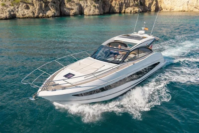 2024 Princess V50 Open yacht cruising in clear blue waters near rocky coastline.