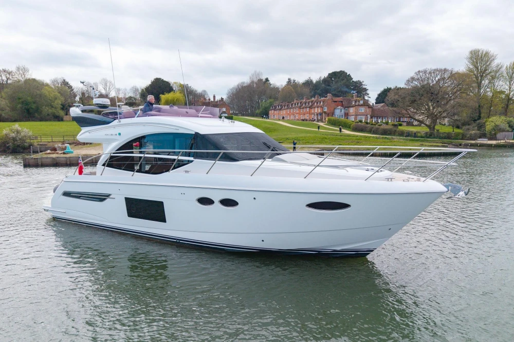 Luxurious 2018 Princess 49 yacht cruising on a serene river near lush greenery.