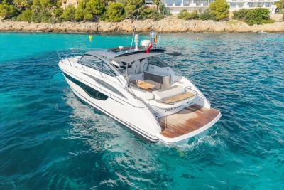 2019 Princess V40 yacht cruising in clear blue waters near a rocky shoreline.