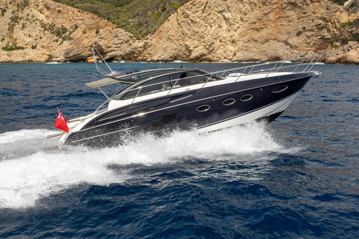 2017 Princess V48 Open yacht cruising on blue ocean near rocky coastline.