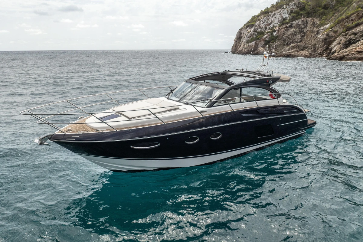 2017 Princess V48 Open yacht cruising near rocky coastline.