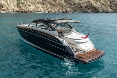 2017 Princess V48 Open yacht cruising in clear blue waters near rocky coastline.