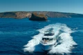 2023 Princess F55 yacht cruising near rocky island in clear blue waters.