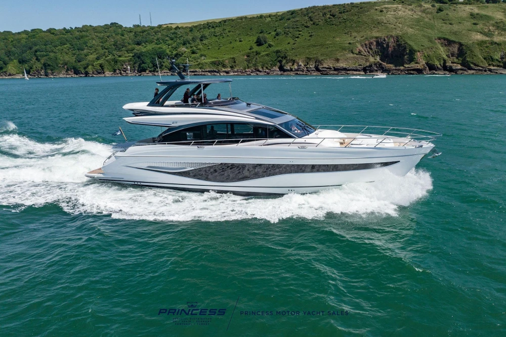 2023 Princess S72 yacht cruising on blue ocean near lush green coastline.