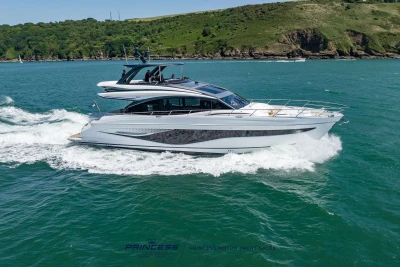 2023 Princess S72 yacht cruising on blue ocean near lush green coastline.