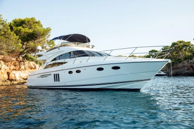 2008 Princess 58 yacht on serene water near rocky shoreline and trees.