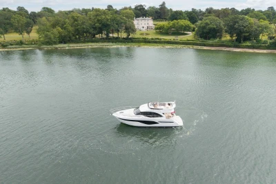 Aerial view of 2026 Princess F50 yacht cruising on a serene lake near a lush estate.