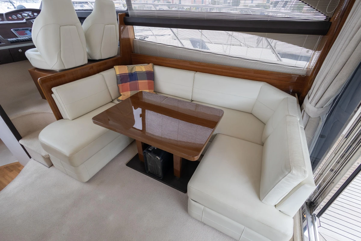 Luxurious interior of 2013 Princess 42 yacht with white leather seating and wooden table.