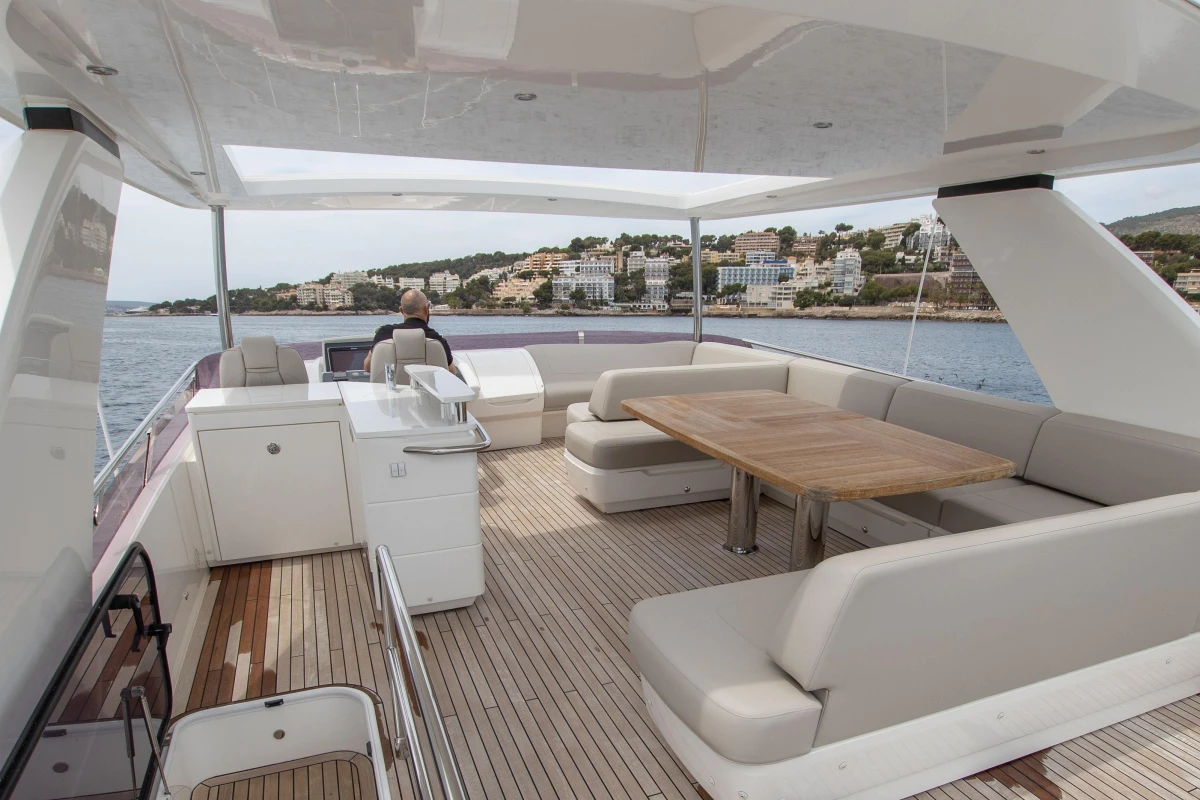 Luxurious 2015 Princess 68 yacht deck with seating and dining area, overlooking coastal scenery.