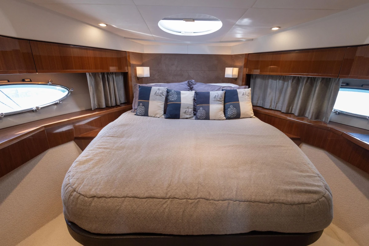 Luxurious cabin interior of 2012 Princess 50 yacht with cozy bedding and elegant wood finish.