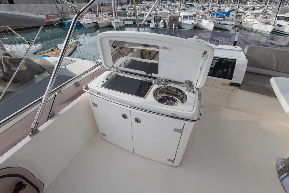 Outdoor kitchenette on 2012 Princess 50 yacht, featuring grill and sink, docked at marina.