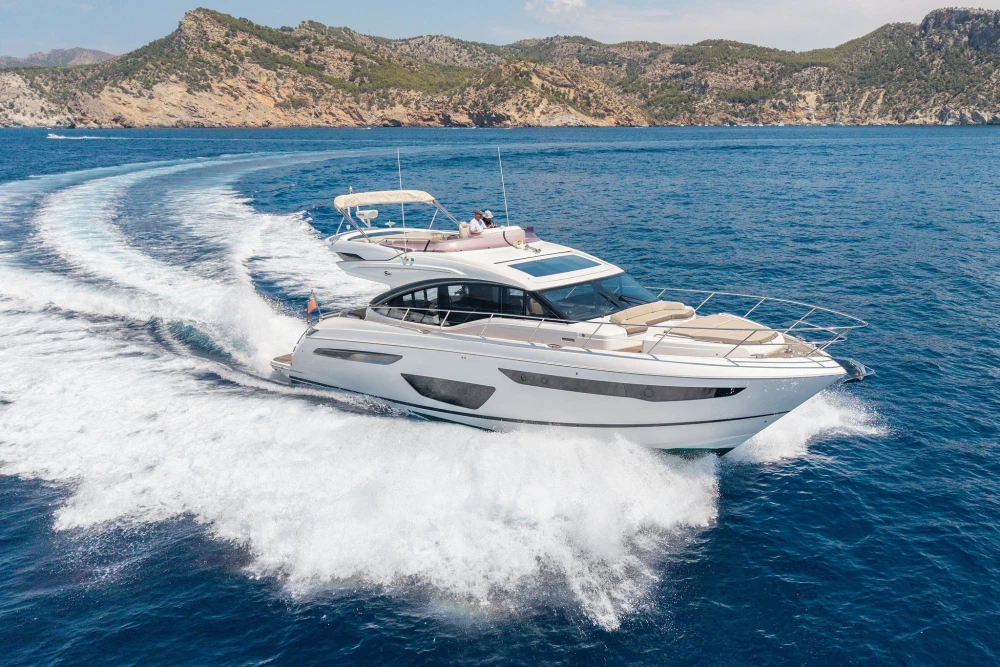 Luxurious 2018 Princess S60 yacht cruising in clear blue waters near rocky coastline.