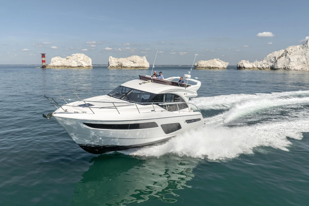 2022 Princess F50 yacht cruising near rocky coastline and lighthouse.