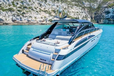 Luxurious 2005 Princess V58 yacht in turquoise waters near rocky coastline.